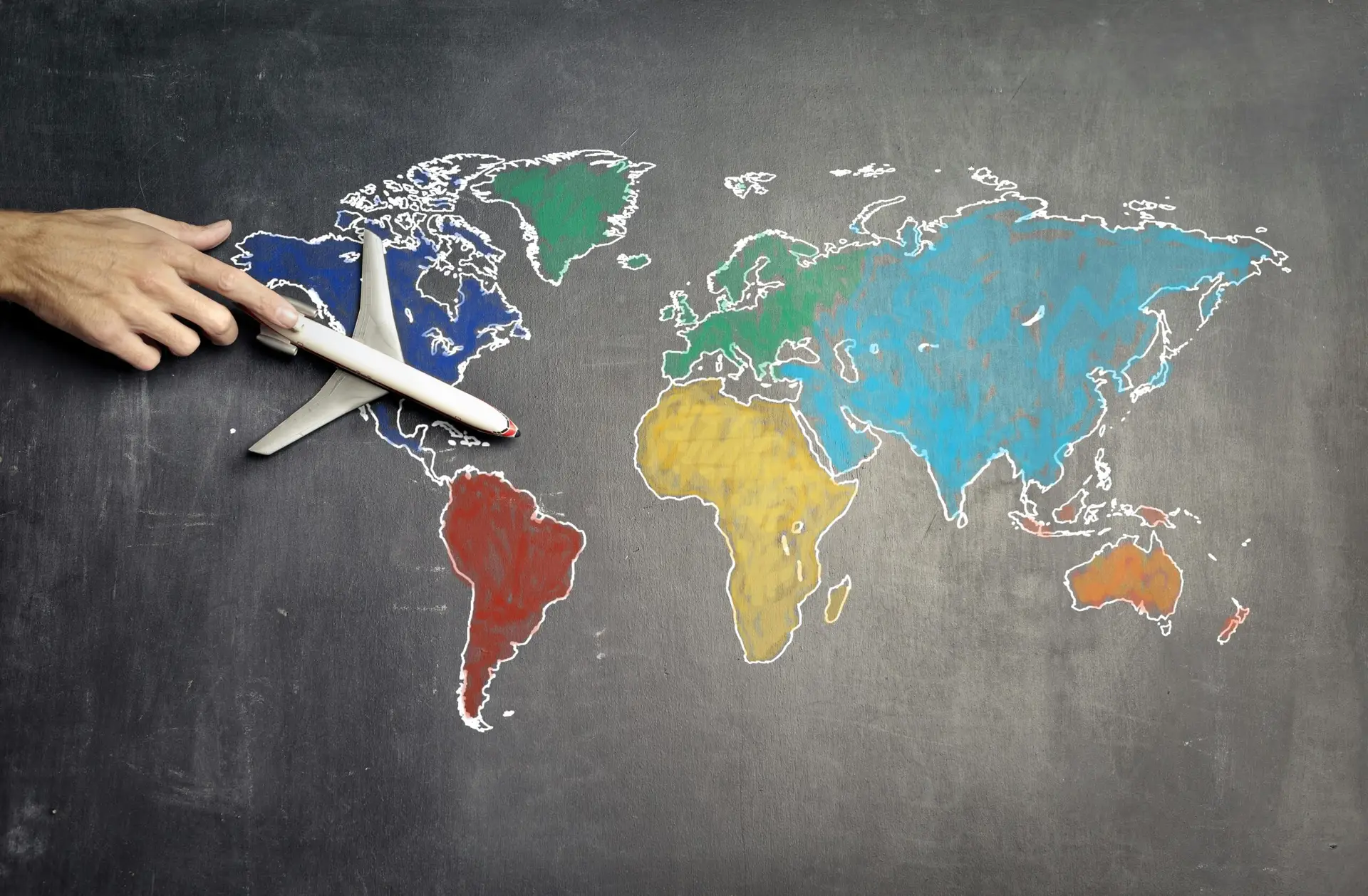 Solutions Top view of crop anonymous person holding toy airplane on colorful world map drawn on chalkboard
