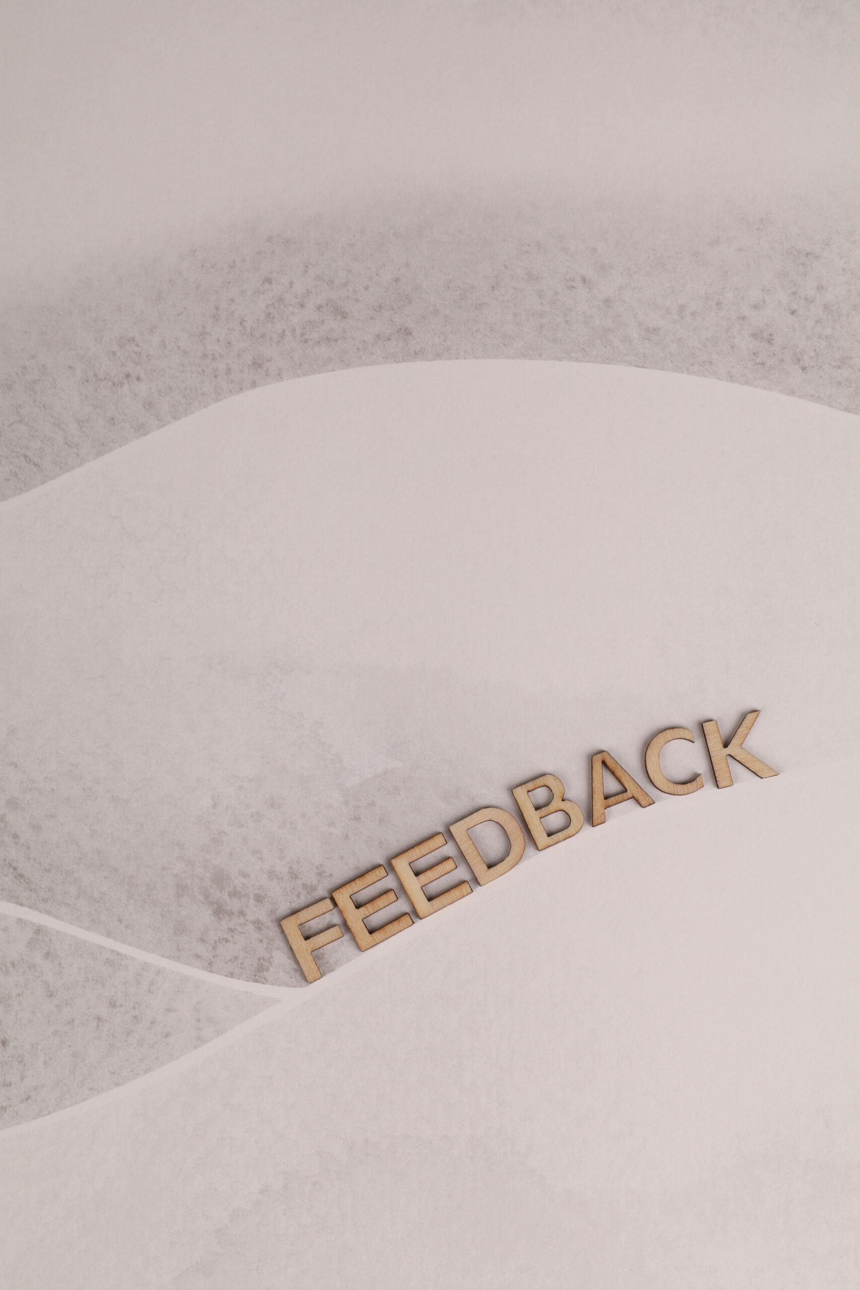 A conceptual image depicting feedback with wooden letters on a minimalist white background.