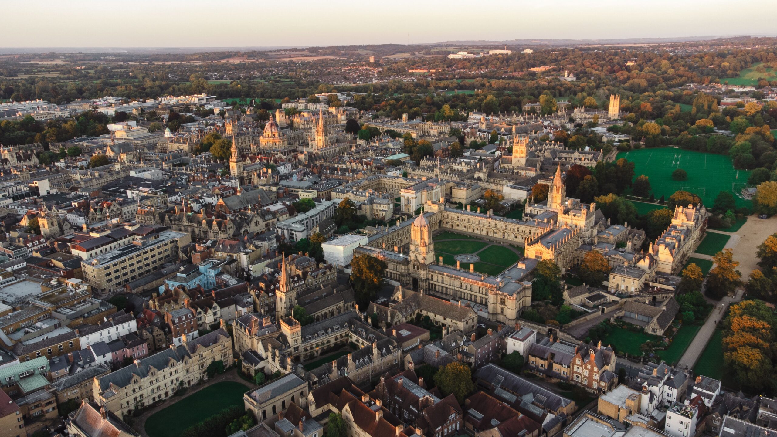 Stunning aerial view of Oxford's historic architecture and green spaces at sunset.